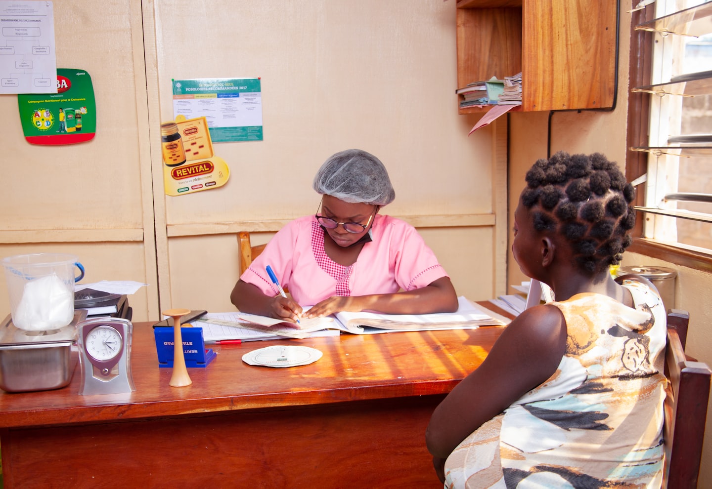 Professional in pink uniform writing in ledger at wooden desk.